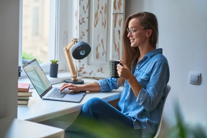 une freelance devant son ordinateur portable en train de boire un café